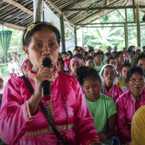 A woman is holding and speaking on a microphone and surrounded by many people all under a tent.
