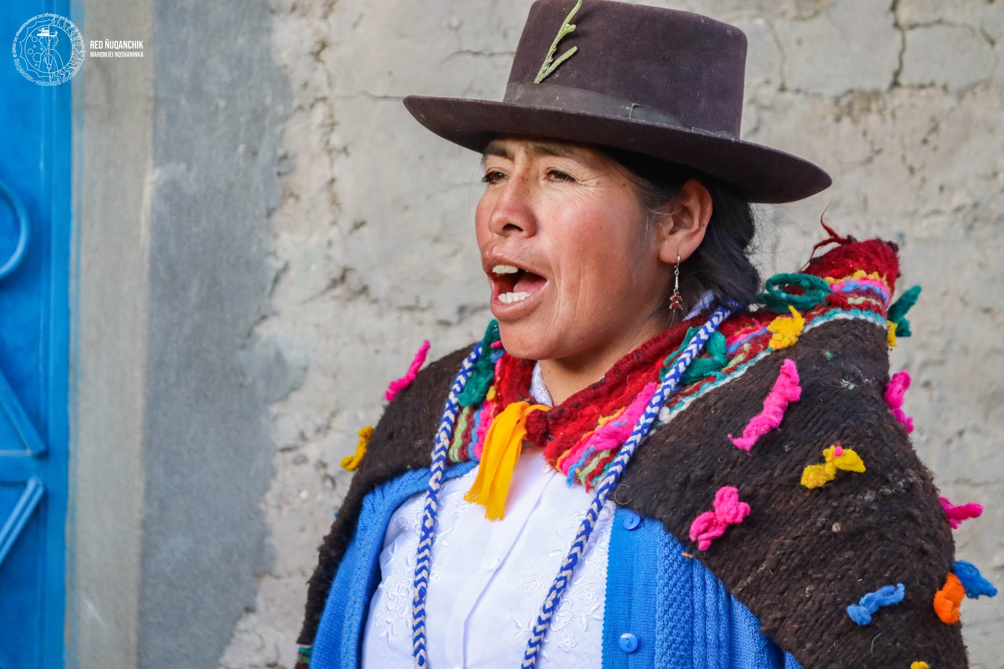 A close up shot of an an Indigenous woman. She is wearing blue cardigan and a multicolored robe on that. She is also wearing a hat and appears to be in the middle of saying something. Picture courtesy of La Red Ñuqanchik Maronijei Noshaninka.