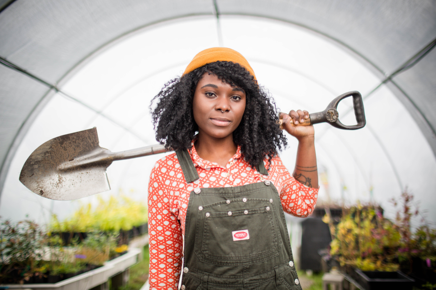 Portrait of a young woman with a shovel in a greenhouse.