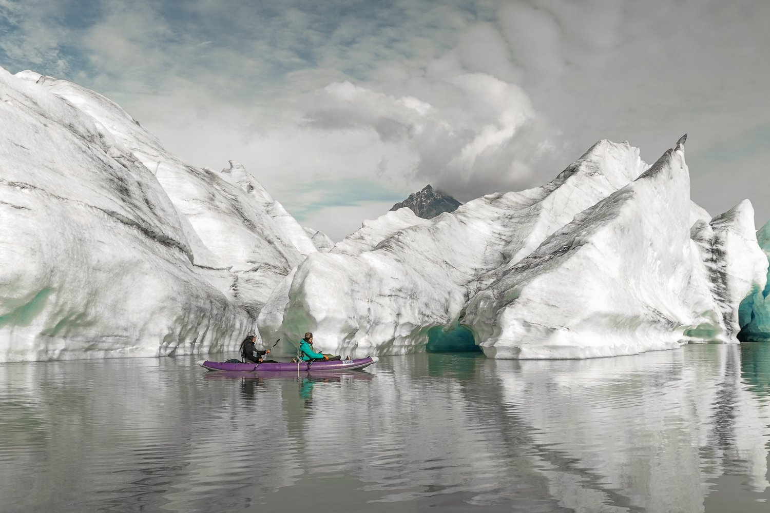 Two people paddling in a small boat in front of the Sheridan Glacier.